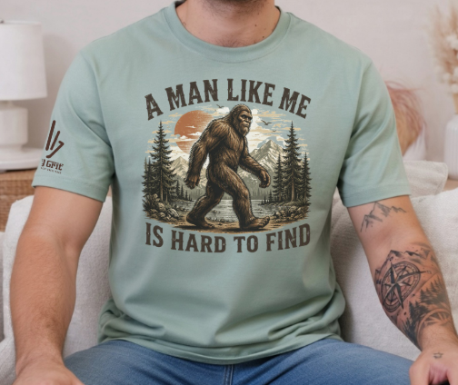 Funny shirt featuring A Man Like Me Is Hard To Find with Bigfoot walking through the woods