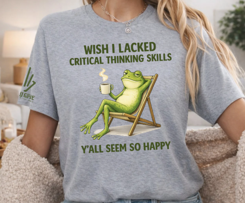 Shirt graphic reading “Wish I Lacked Critical Thinking Skills, Y'all Seem So Happy” with a frog sitting in a chair holding coffee.